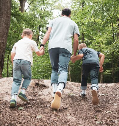 Vater mit zwei Söhnen auf Waldweg in Barfußsocken und Barfußschuhen